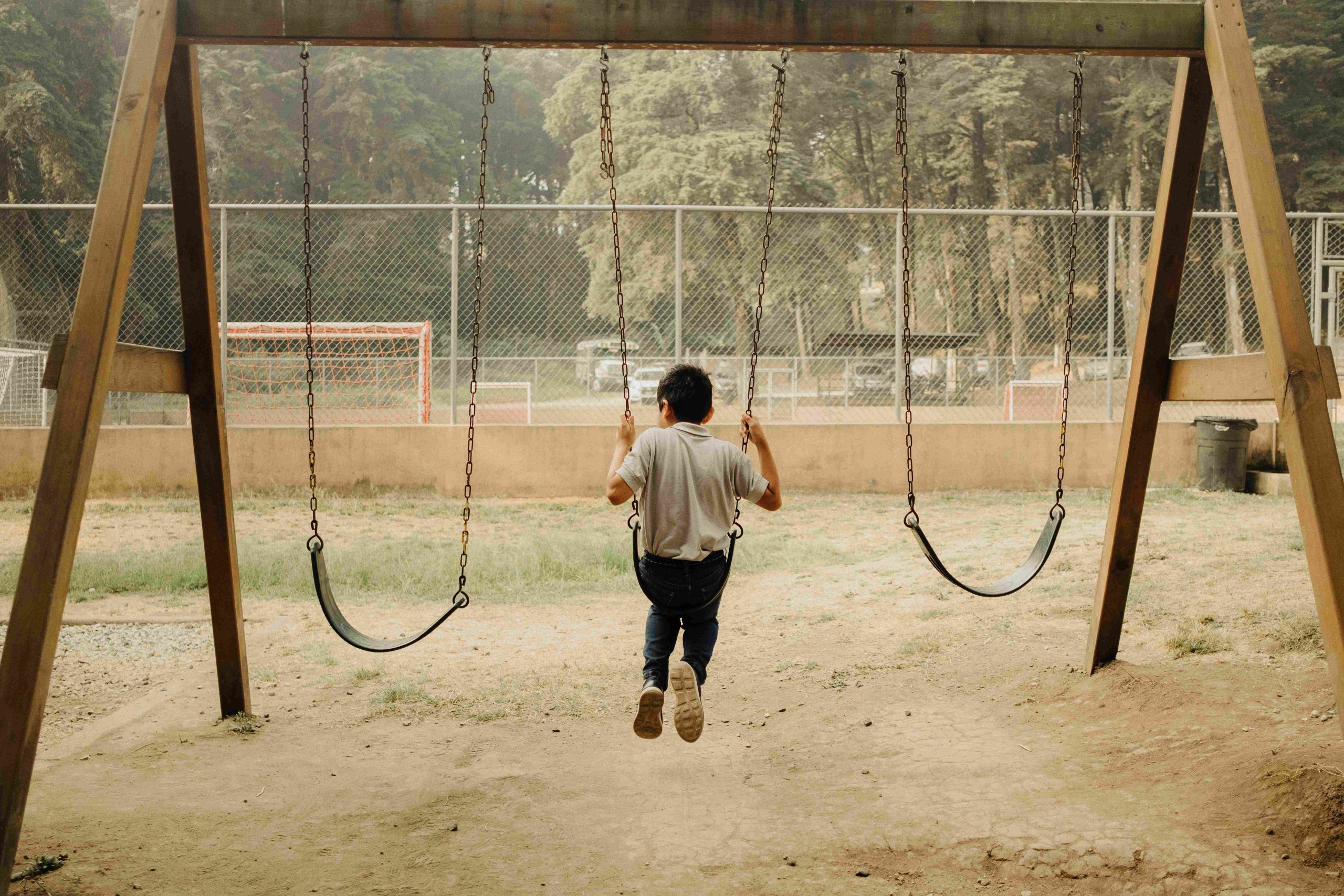 En pojke sitter på en gunga på en fotbollsplan.